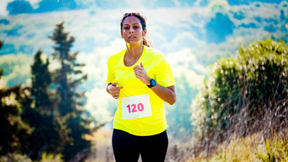 Image of a female jogger in a yellow shirt with a fitness tracker and sports headphones.