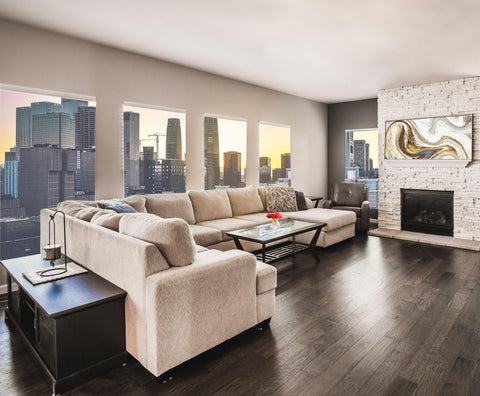 This is a picture of a modern living room with a large tan sectional sofa on a brown hardwood floor with the image of a city skyline outside. Find it at knecthome.myshopify.com